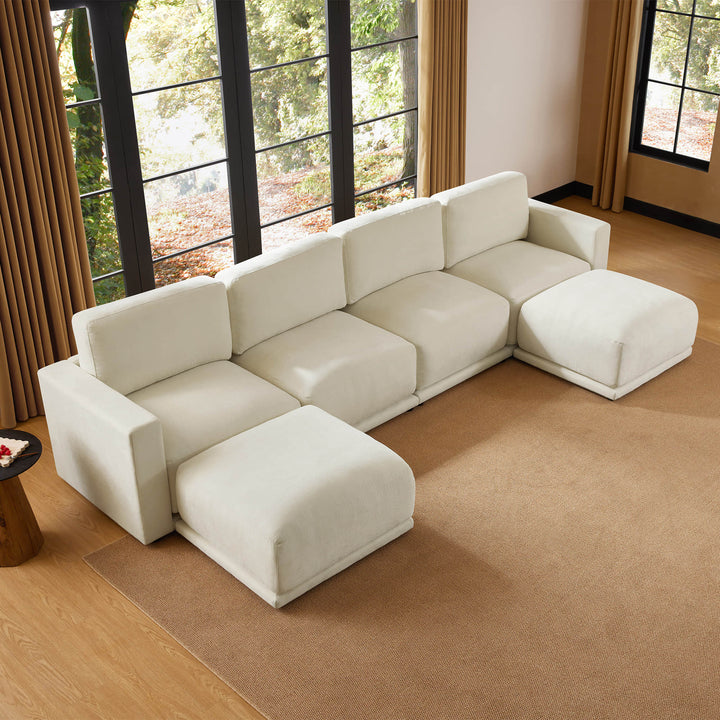 Aerial view of a modern sectional sofa with a minimalist design, set in a cozy room with large windows and a natural color palette.