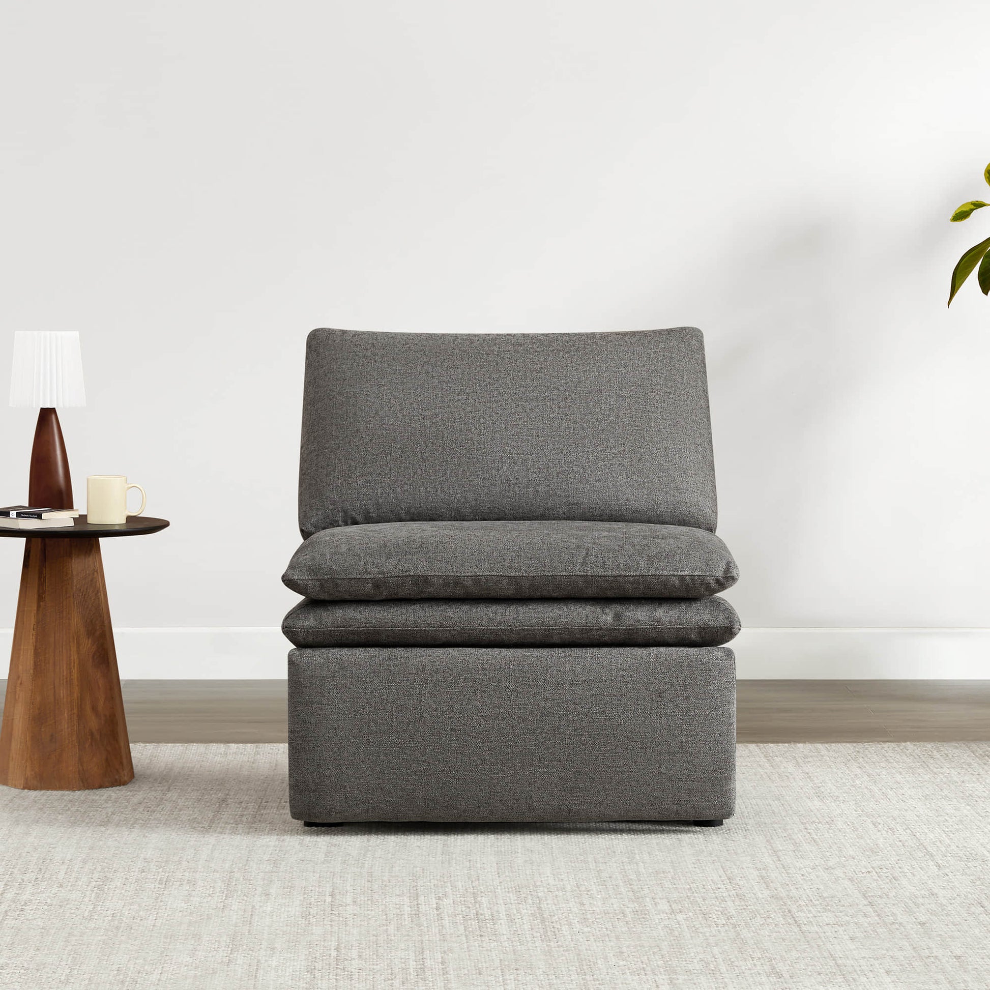 Contemporary gray armless recliner with plush cushions beside a coffee table and lamp.