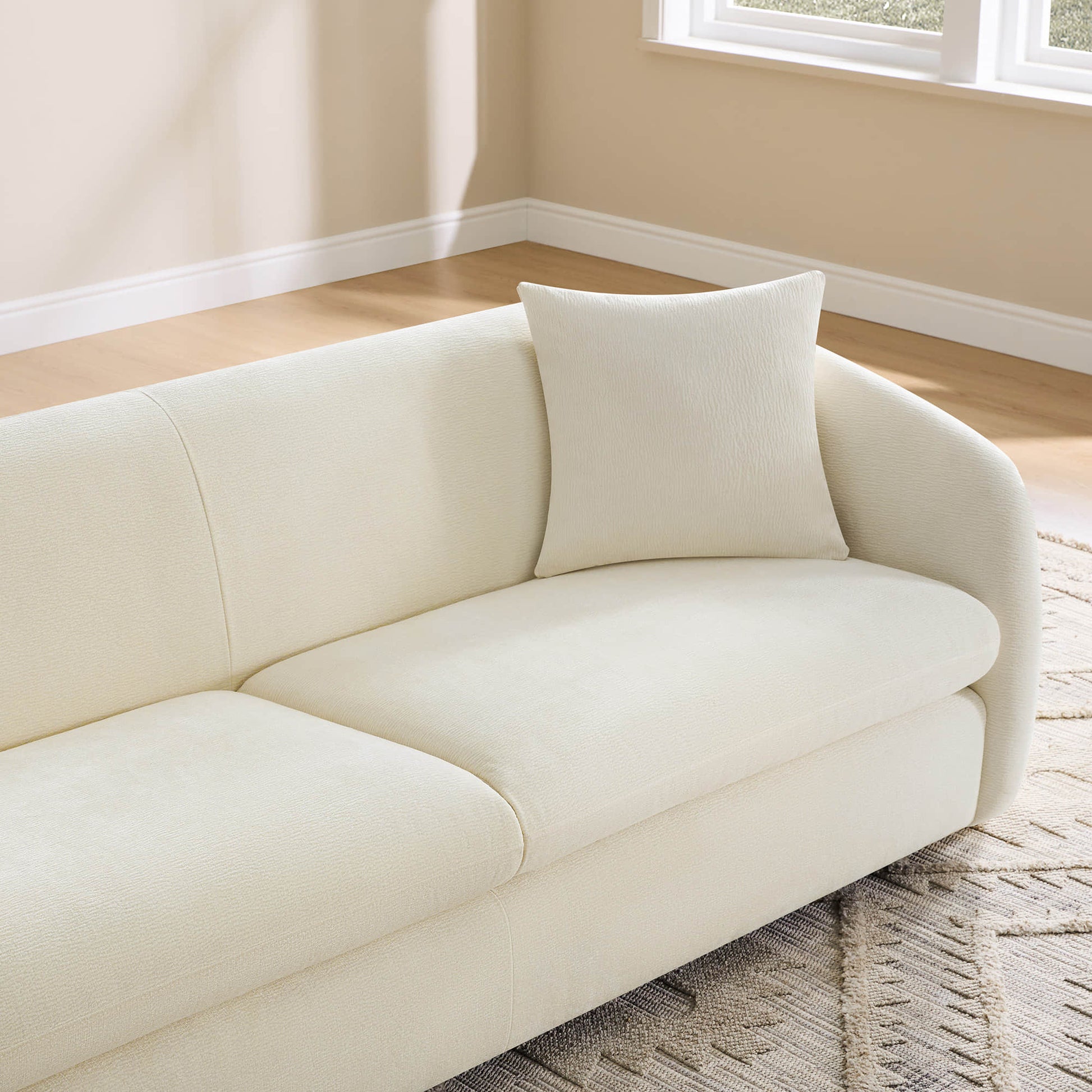 A close-up of a cream modern sofa with a matching pillow, highlighting its elegant design and soft texture.
