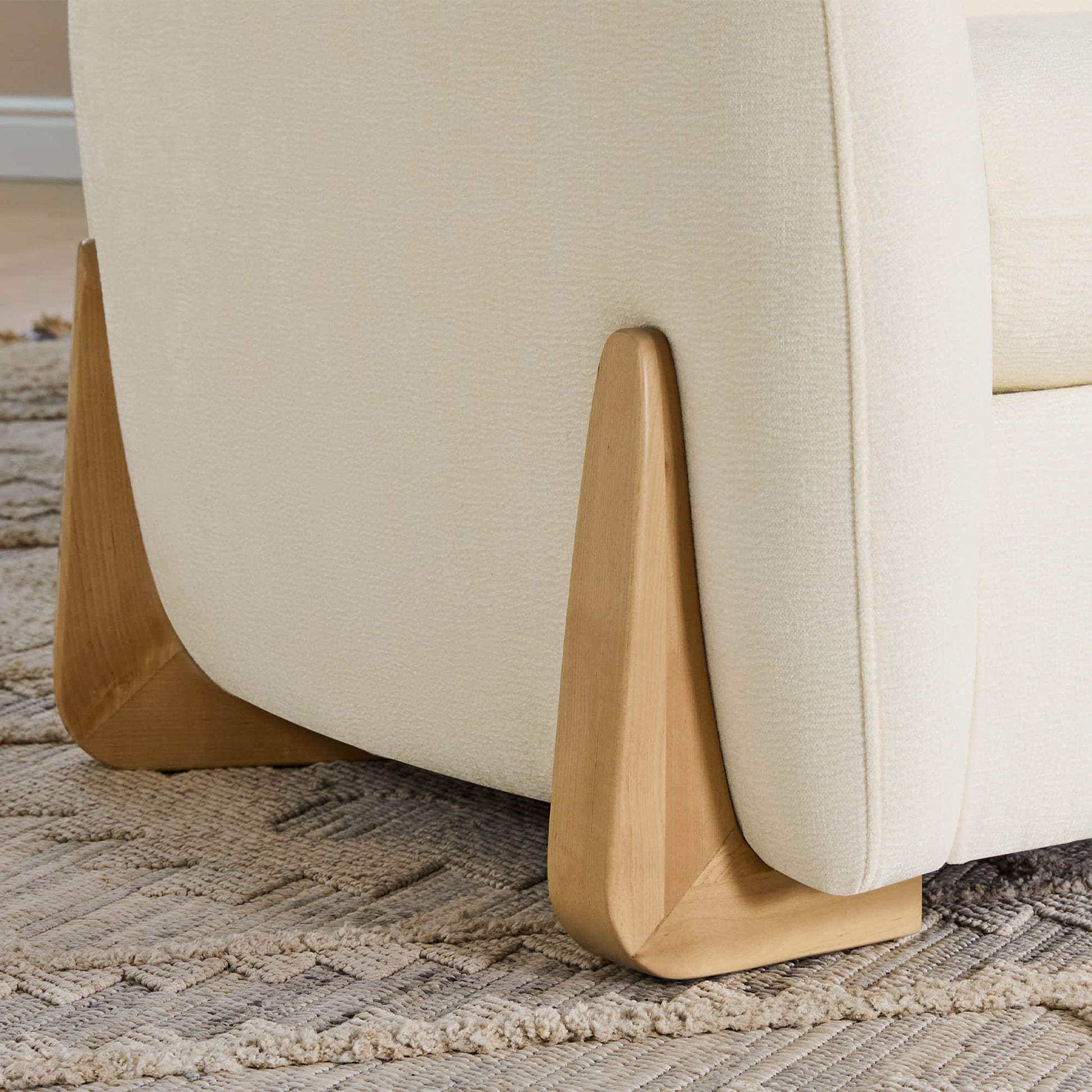 A close-up of a cream modern sofa featuring wooden accents on the legs, highlighting its stylish design and craftsmanship.