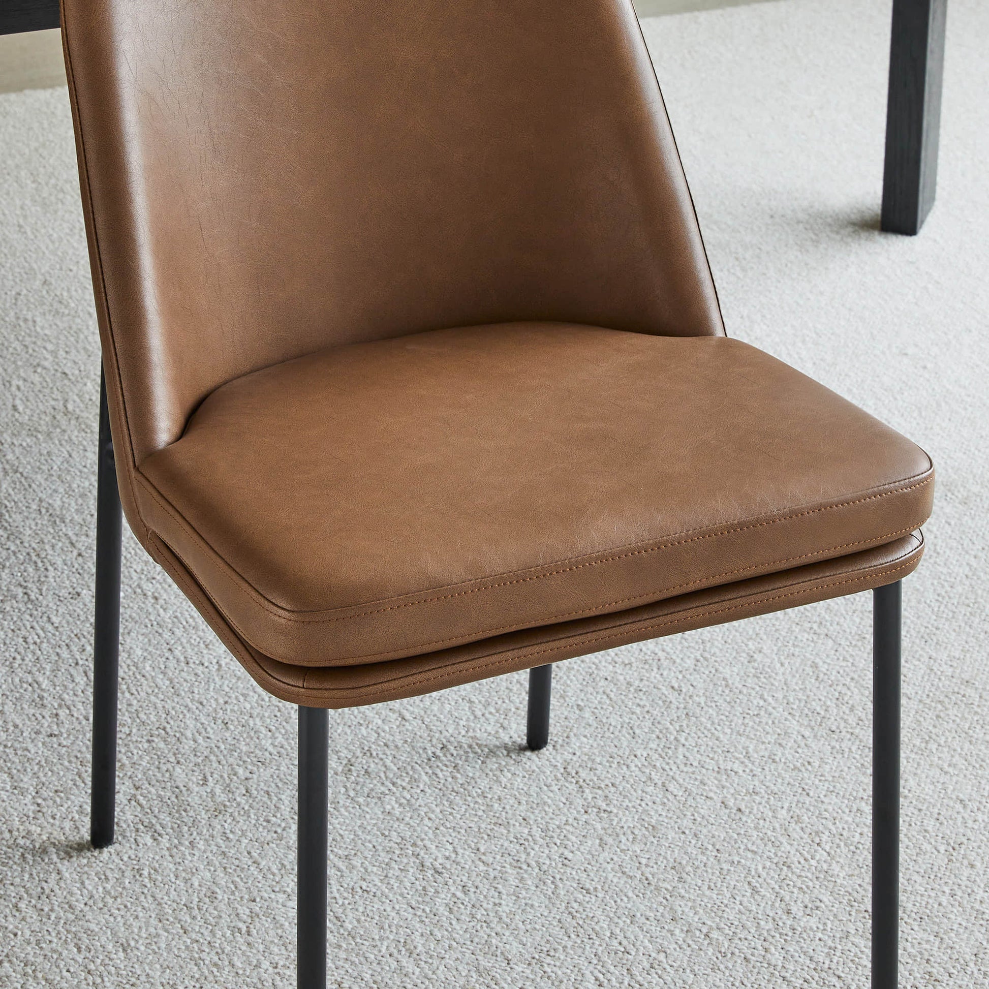 Golda Dining Chair, brown leather with black metal legs, close-up of seat and partial backrest.