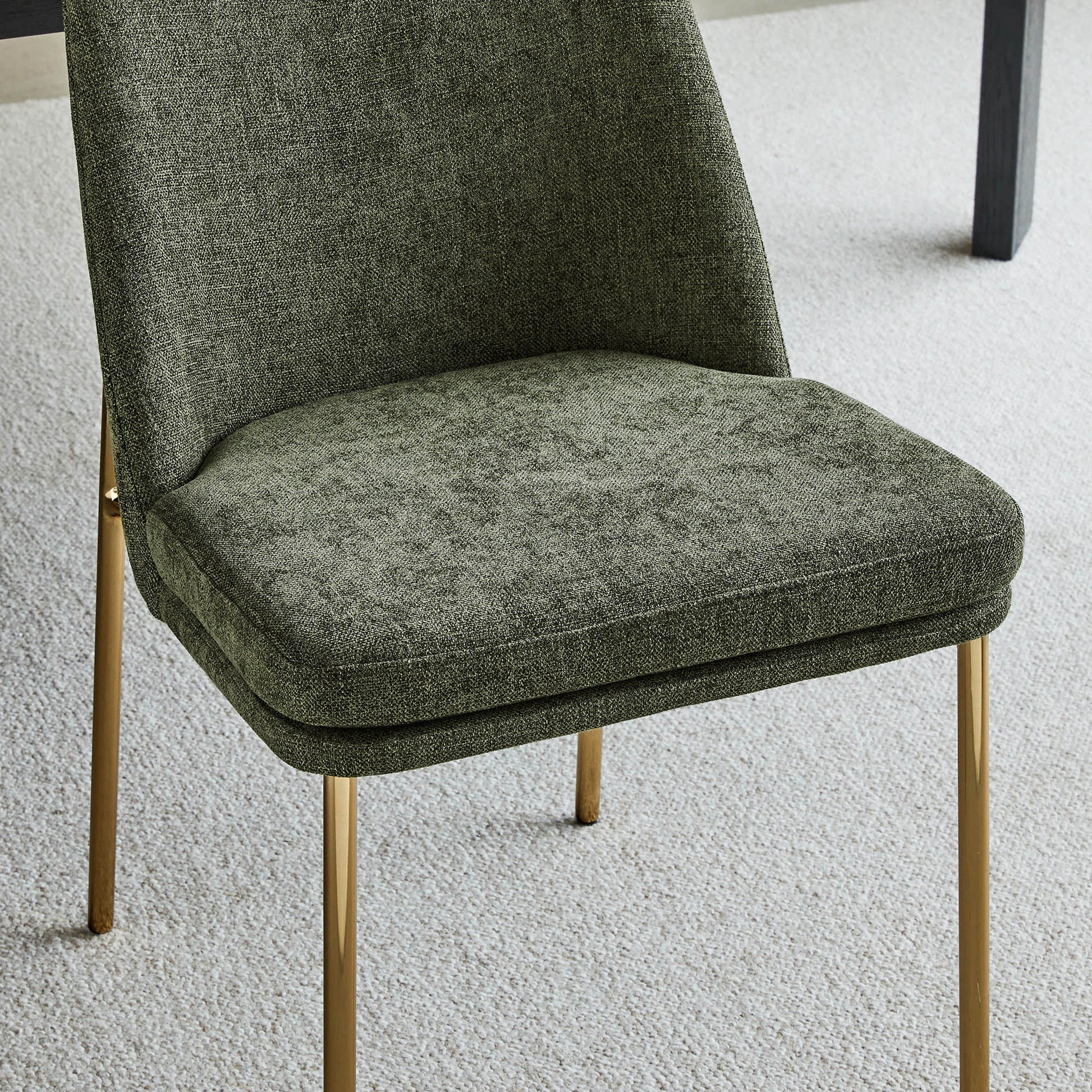 Golda Dining Chair, green fabric with gold legs, close-up of seat and backrest in a carpeted room.