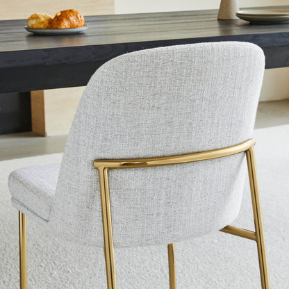 Golda Dining Chair, light gray fabric with gold legs, back view in a modern dining setting.