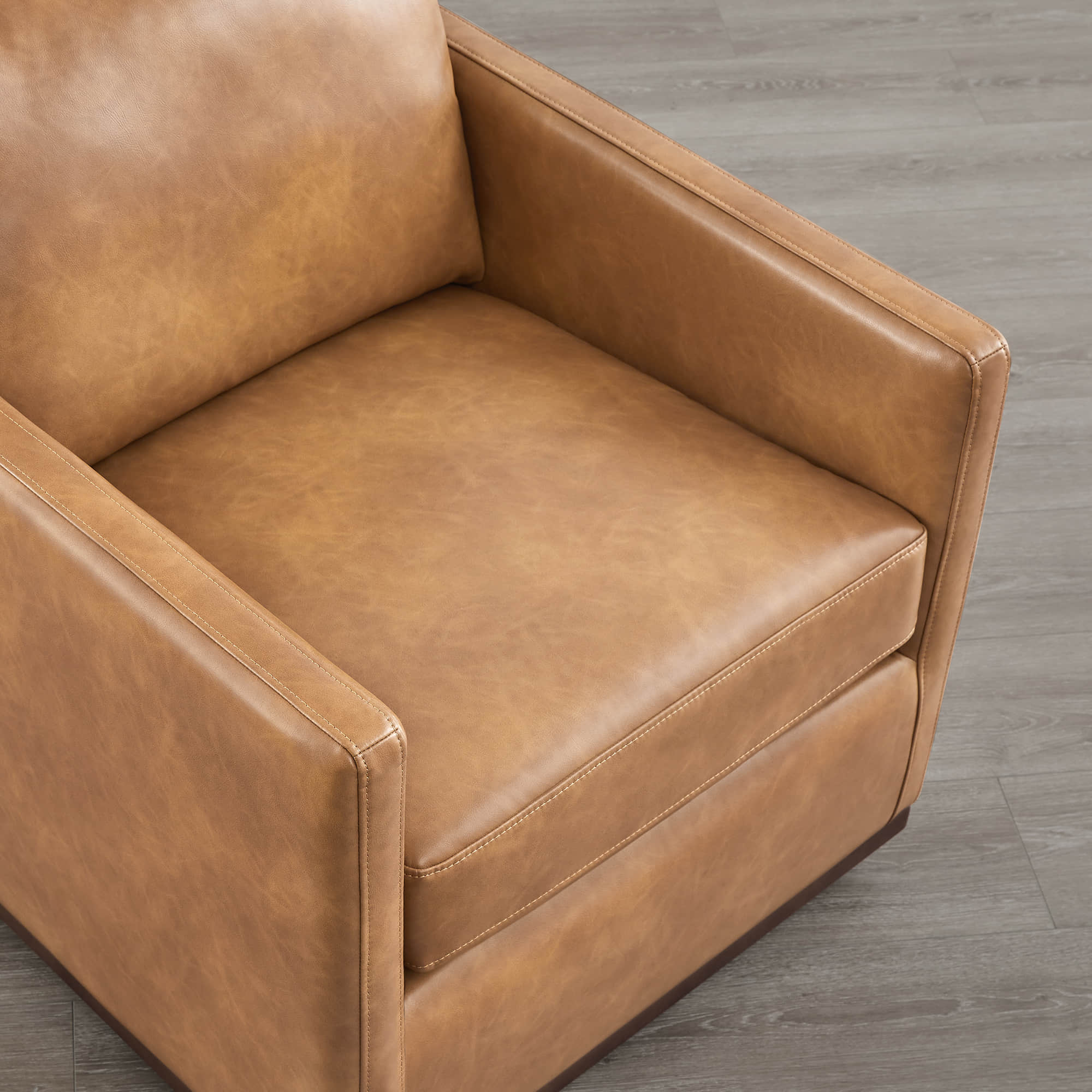 Detail view of Henry Modern Swivel Accent Chair's tan leather cushion and wooden base - CHITA Living