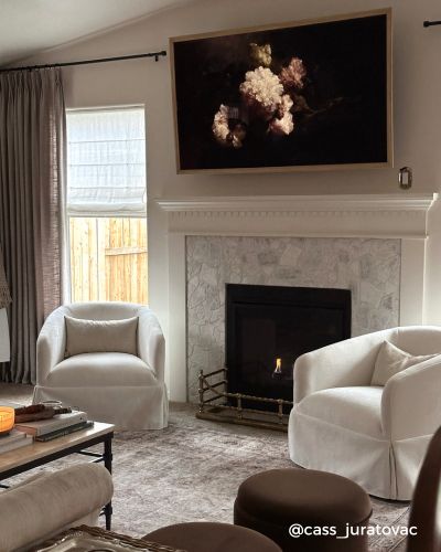 A cozy living room with a lit fireplace, two white armchairs
