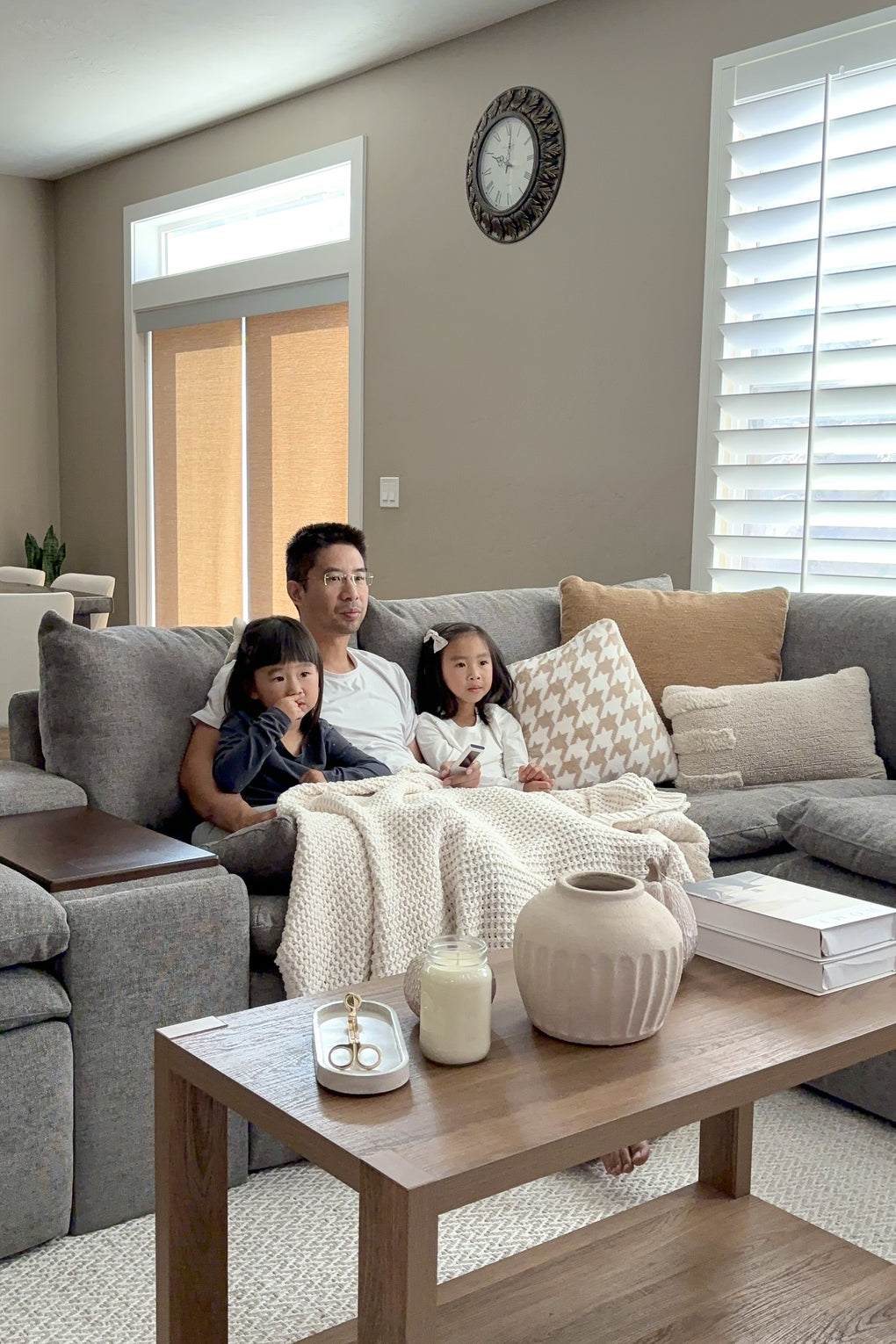 Family seated on a gray modular sofa around a wood coffee table, showing a comfortable living room setup for everyday togetherness and shared downtime at home.