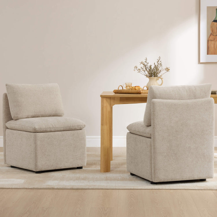 Two beige linen minimalist armless dining chairs with plush cushions beside a light wood table.