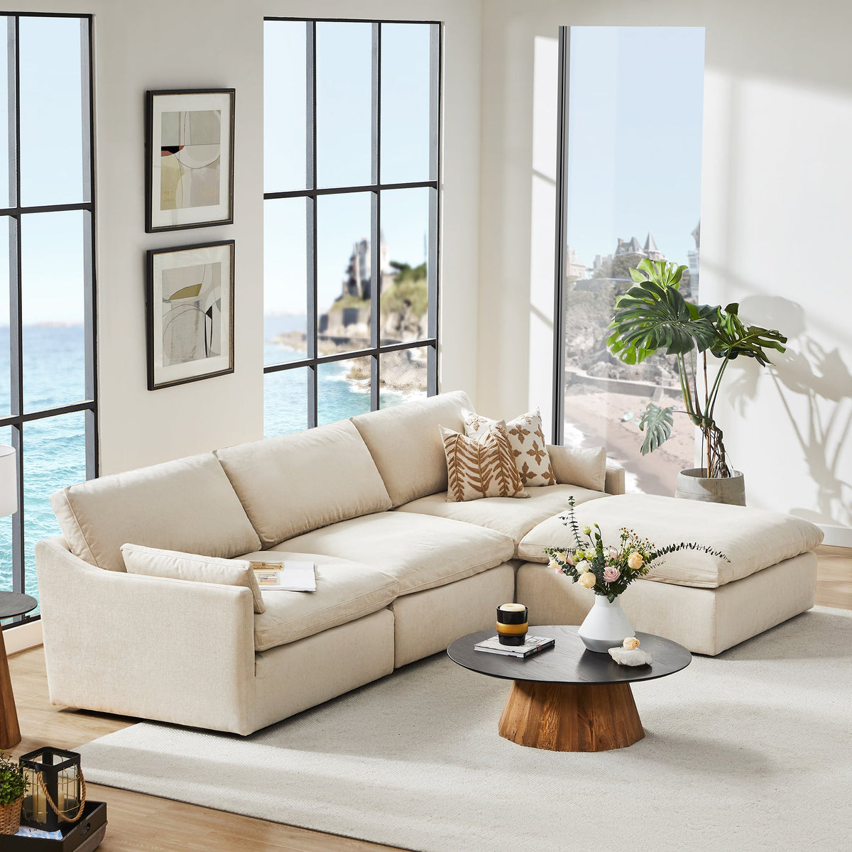 Kenna sectional in Cream with brown patterned pillows, a dark round table and pale walls beside large windows.